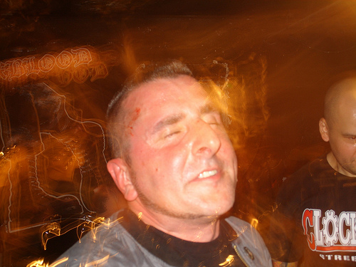 Flash candid of a man mid-song at a basement show, light streaking