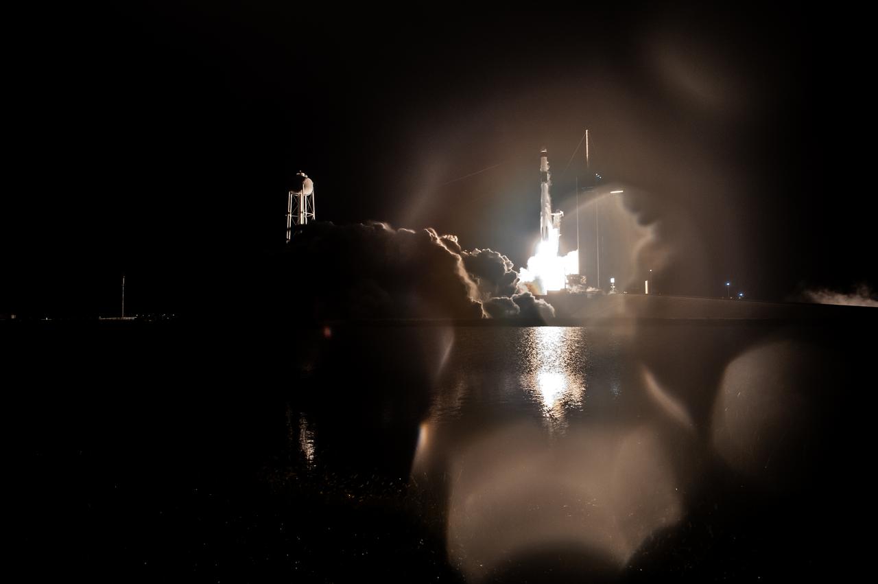 SpaceX rocket lifting off at night through blurred foreground