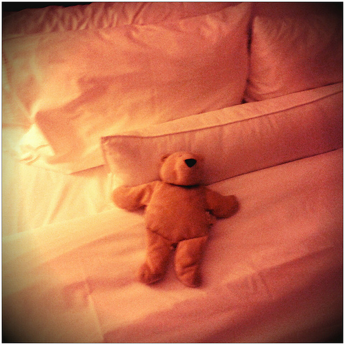 Teddy bear on a motel bed in warm orange light
