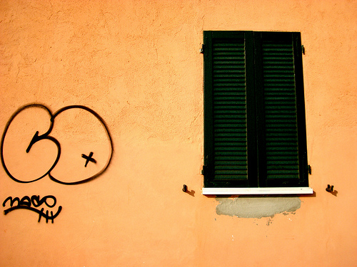 Peach wall with black shutters and a graffiti tag