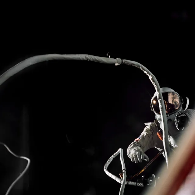 An astronaut tethered to a spacecraft against the darkness of space.