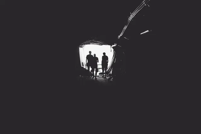 Silhouetted people at a bright opening surrounded by darkness.