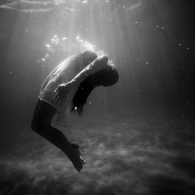 A person floating underwater beneath shafts of light.