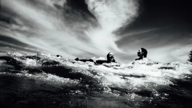 Figures in the ocean beneath dramatic light and clouds.